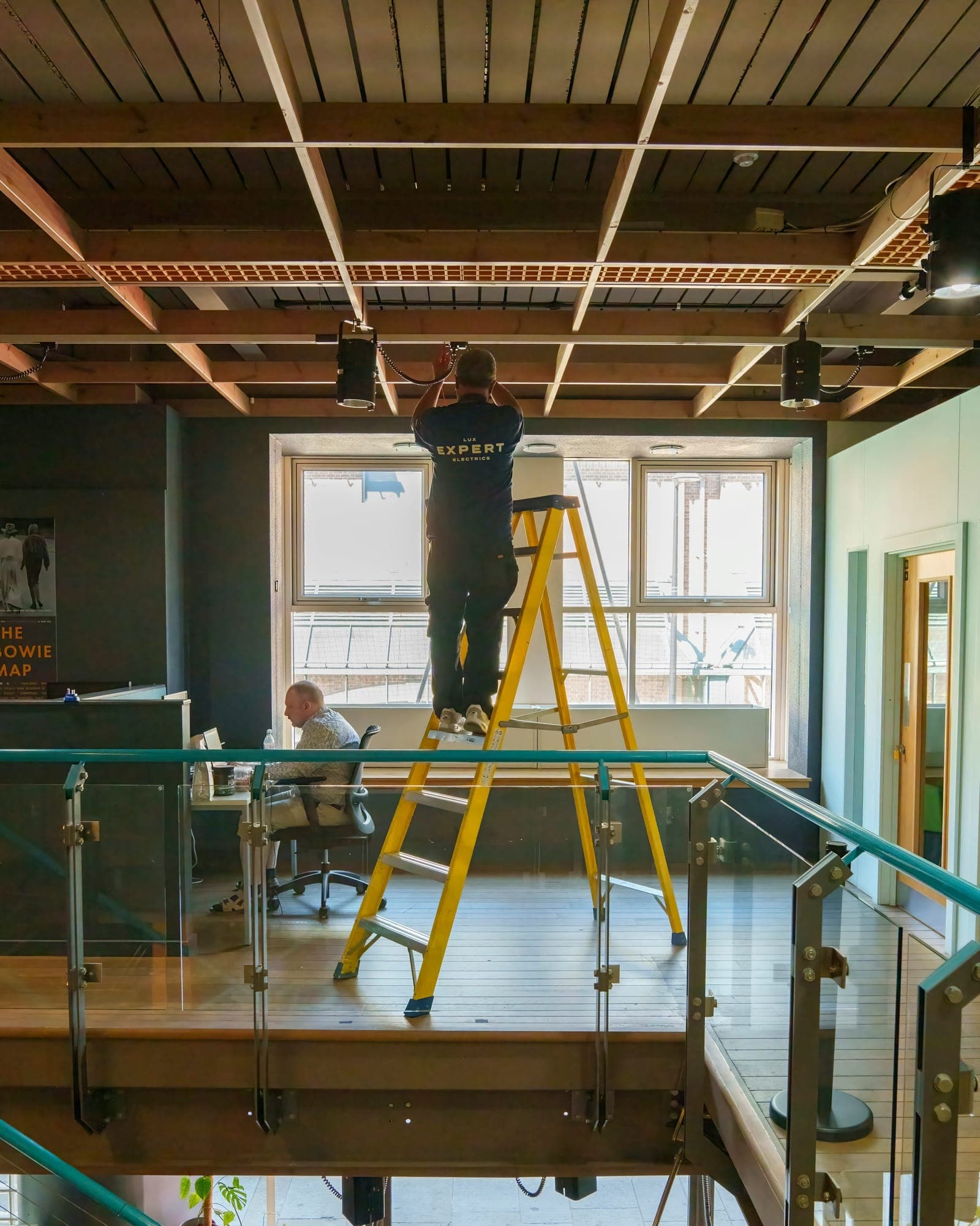 Electrician on a ladder installing ceiling lights in an open office