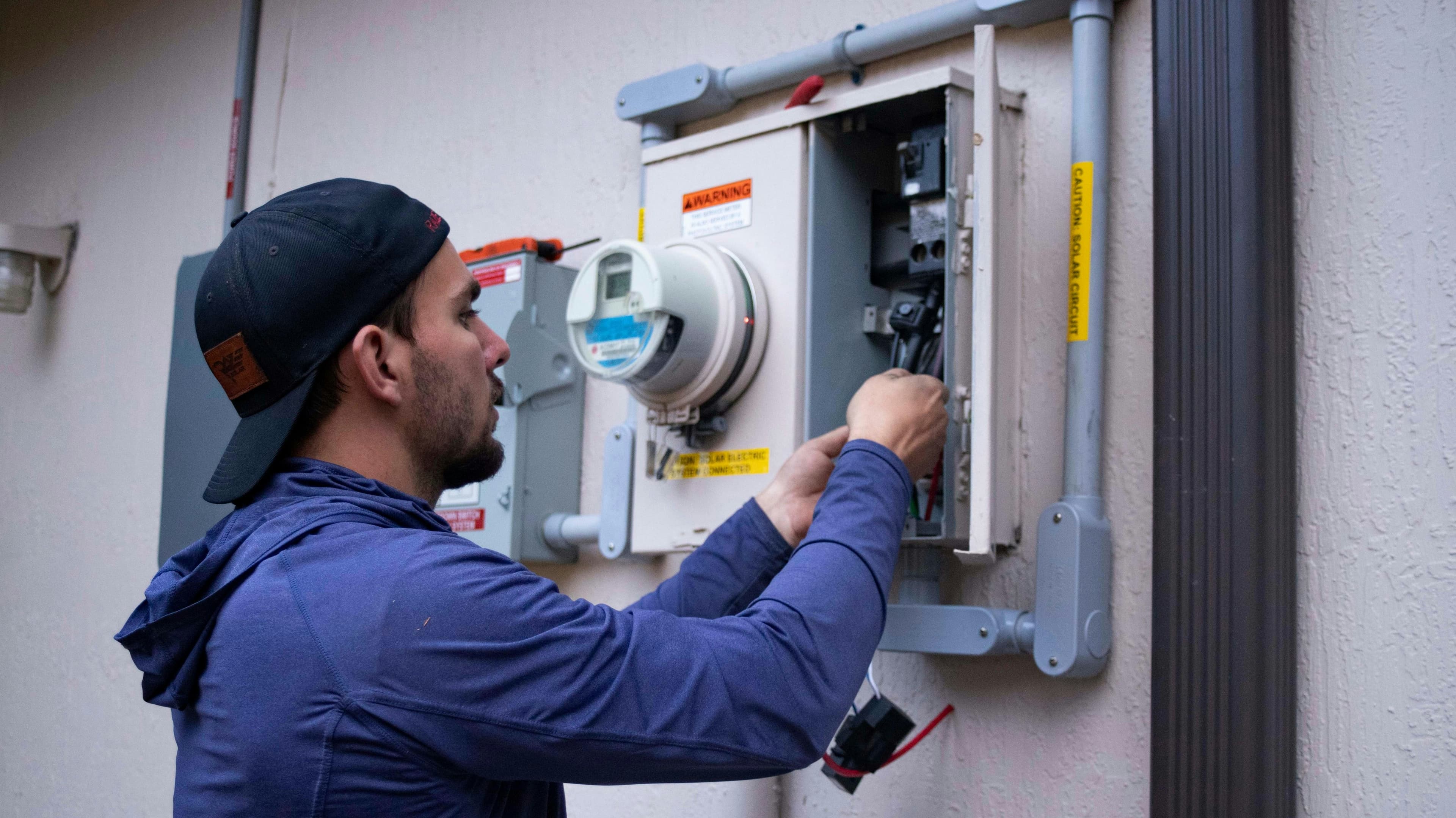 Electrician in work gloves testing a home electrical panel with a multimeter